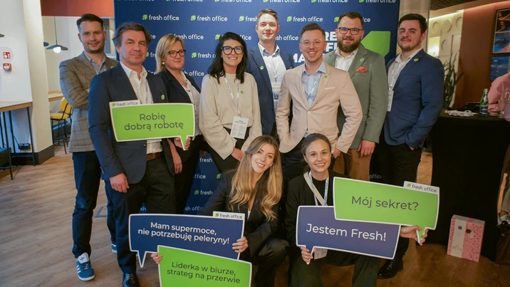 Zespół Fresh Office prezentujący tabliczki z hasłami motywacyjnymi na tle firmowego banera podczas wydarzenia