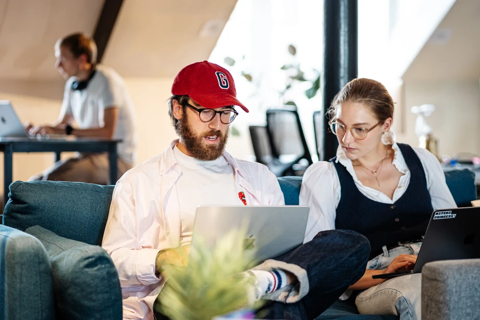 Dwóch pracowników w casualowym biurze współpracuje na laptopach siedząc na kanapie w nowoczesnym open space