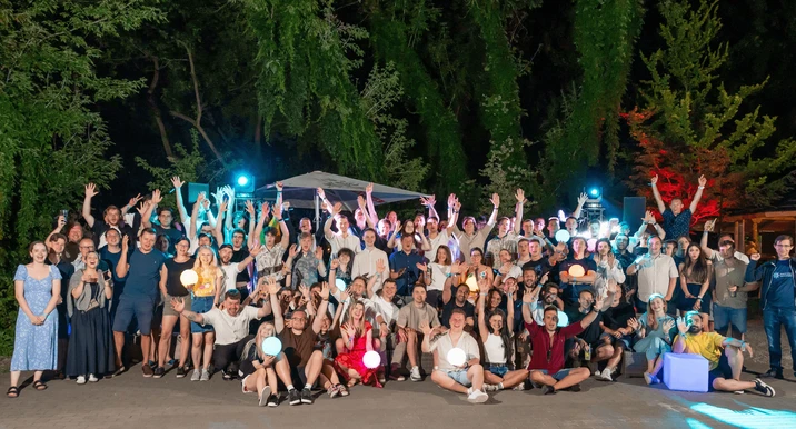 Duża grupa pracowników podczas nocnego firmowego spotkania na świeżym powietrzu z rozświetlonymi kulami i uśmiechami