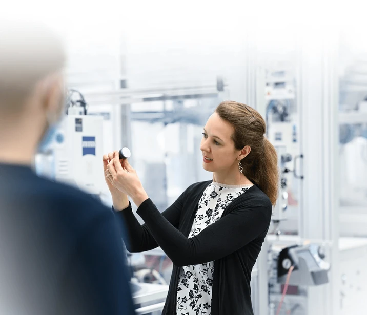 Kobieta prezentuje produkt lub element techniczny w nowoczesnym zakładzie produkcyjnym podczas rozmowy z współpracownikiem