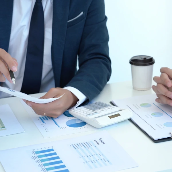 Dwóch biznesmenów analizuje raporty finansowe przy biurku z kalkulatorem i kawą w firmowym biurze