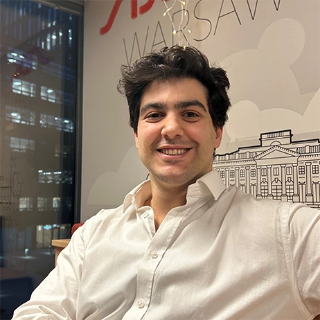 Młody mężczyzna w białej koszuli uśmiecha się w nowoczesnym biurze z widokiem na miasto