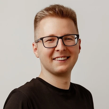 Młody mężczyzna w czarnym t-shircie i okularach uśmiecha się na jasnym tle w profilu pracodawcy