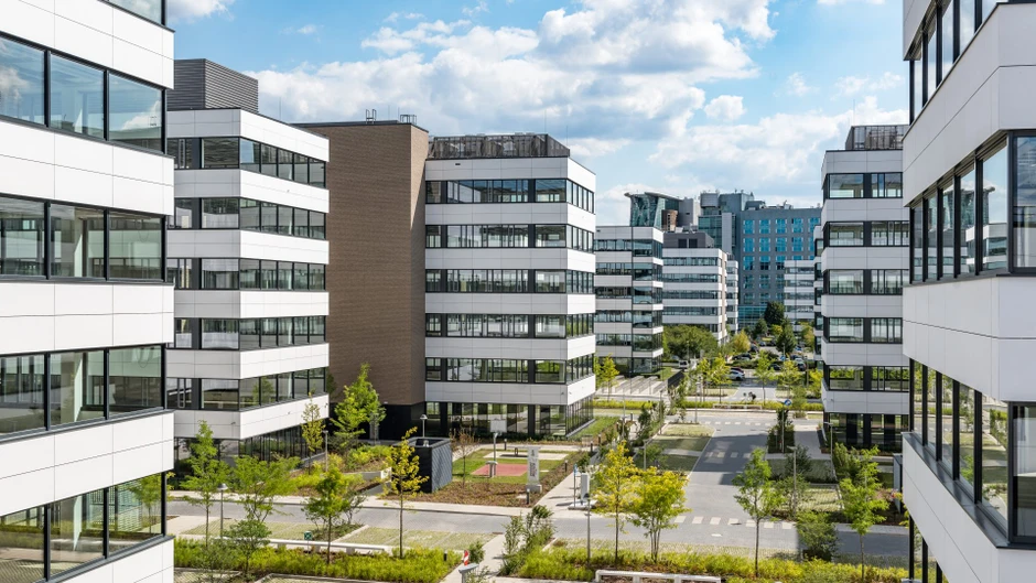 Nowoczesny kompleks biurowy z zielonymi przestrzeniami i szklanymi fasadami na tle nieba