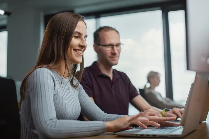 Zespół pracowników współpracuje przy projektach w jasnym biurze z dużymi oknami i nowoczesnym sprzętem