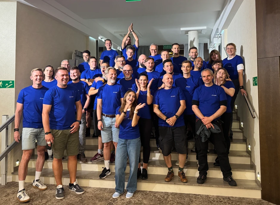 Zespół pracowników w niebieskich koszulkach stoi na schodach, uśmiechnięci i zintegrowani