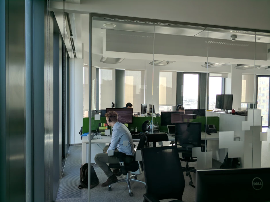 Nowoczesne biuro z pracownikami przy komputerach, jasne wnętrze i duże okna z roletami