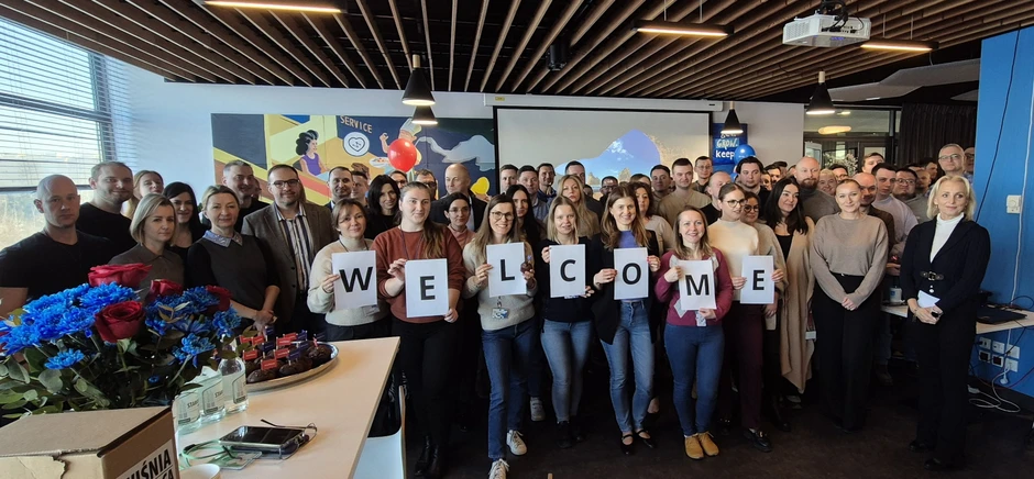 Zespół pracowników w biurze trzymający kartki z napisem WELCOME, witając nowych członków firmy