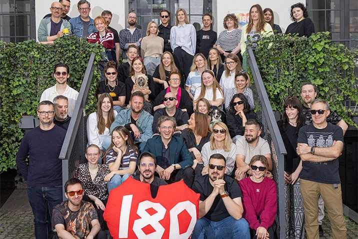 Grupa pracowników firmy zgromadzona na schodach budynku z zielenią, wspólne zdjęcie zespołowe