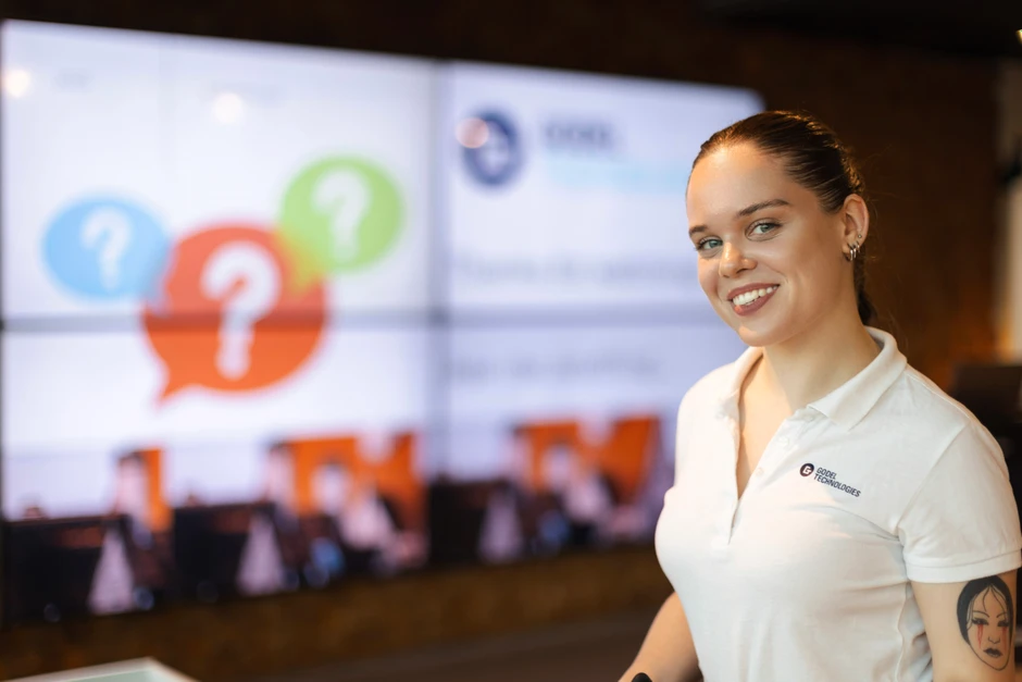 Uśmiechnięta kobieta w białej koszulce z logo Godel Technologies na tle ekranu prezentacyjnego firmy