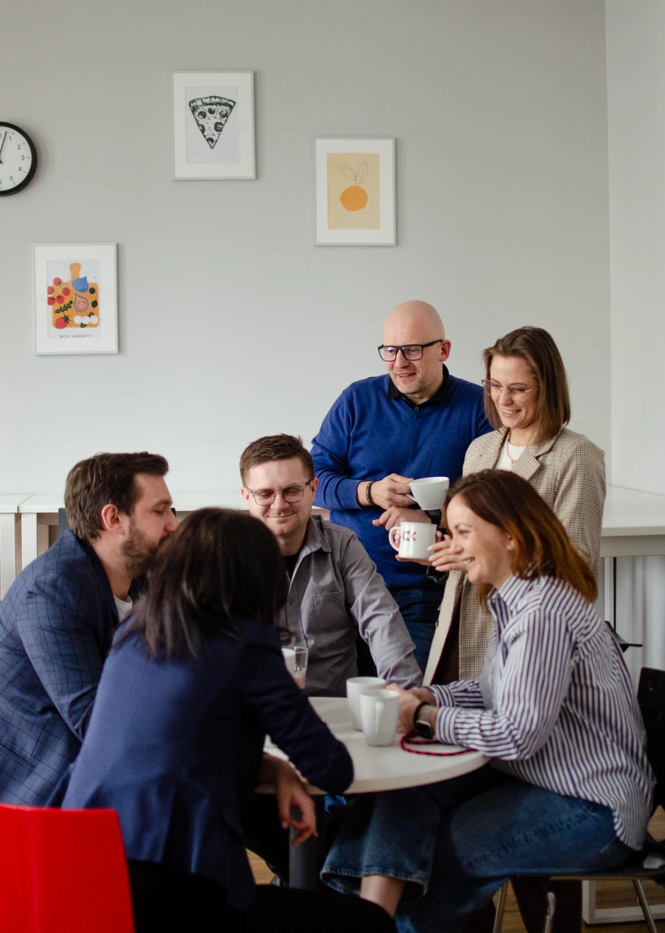 Zespół pracowników spotyka się przy stole na przerwie kawowej w jasnym, nowoczesnym biurze