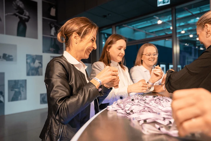 Zespół kobiet zakłada opaski identyfikacyjne podczas firmowego wydarzenia w nowoczesnym wnętrzu