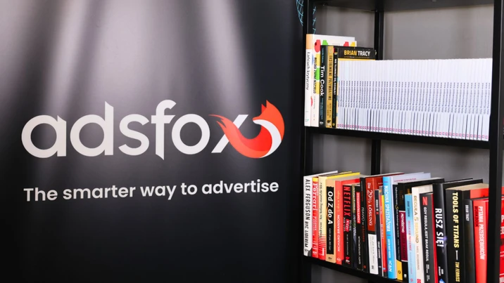 Logo firmy adsfox z hasłem promocyjnym widoczne obok regału pełnego książek biznesowych i marketingowych