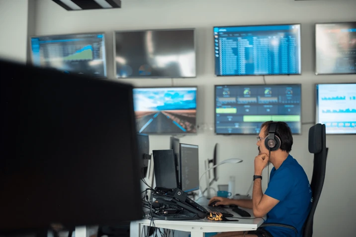 Programista w słuchawkach pracuje w biurze nad wieloma monitorami z danymi i wykresami