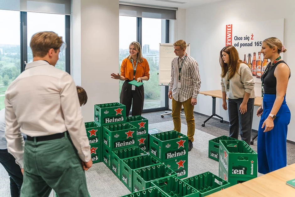 Grupa pracowników podczas integracyjnego zadania zespołowego z użyciem zielonych skrzynek Heineken w nowoczesnym biurze