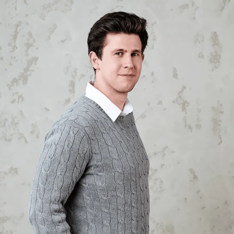 Młody mężczyzna w szarym swetrze i białej koszuli pozujący na jasnym tle do zdjęcia profilowego