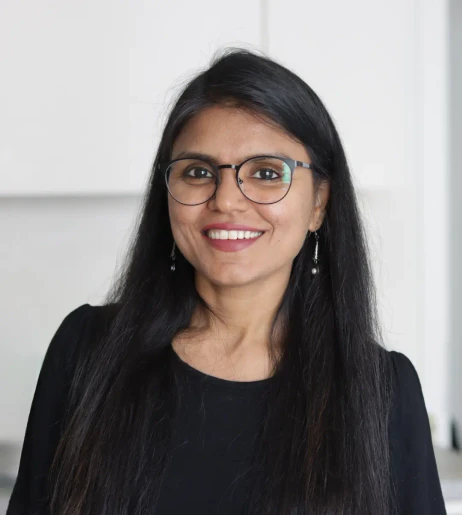 Uśmiechnięta kobieta w okularach i czarnym ubraniu pozująca na neutralnym tle w biurze