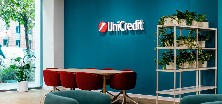 Nowoczesna sala konferencyjna UniCredit z czerwonymi krzesłami i zielonymi roślinami na tle niebieskiej ściany