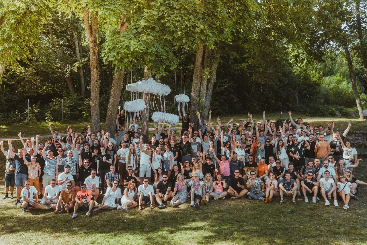 Duża grupa pracowników na firmowym pikniku na świeżym powietrzu w otoczeniu zieleni i ozdobnych chmur