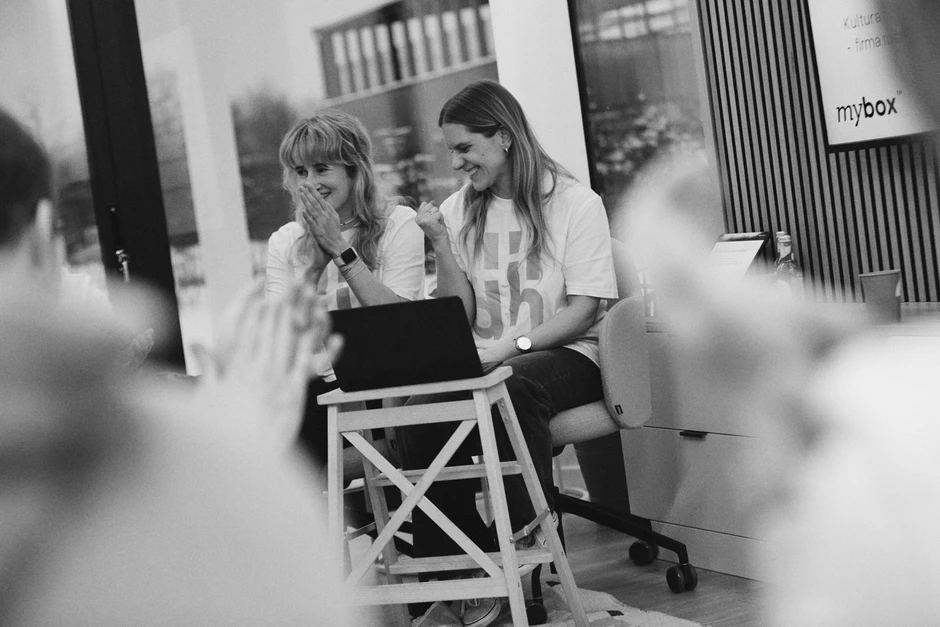 Dwie uśmiechnięte kobiety podczas spotkania w nowoczesnym biurze na tle laptopa i okna