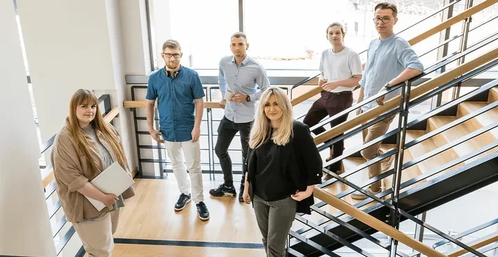 Zespół sześciu młodych profesjonalistów pozujących na nowoczesnych schodach w jasnym biurze