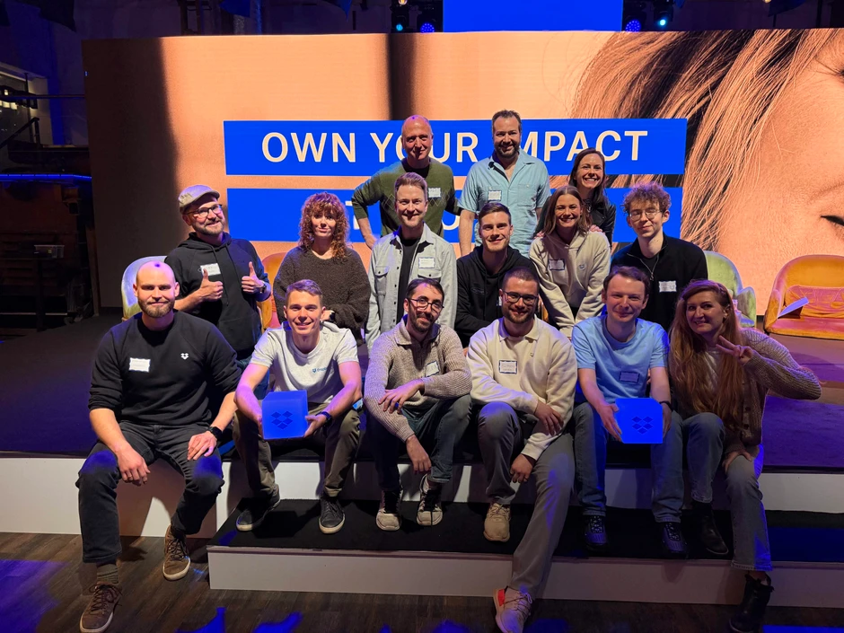 Zespół pracowników podczas wydarzenia firmowego na scenie z napisem Own Your Impact w tle