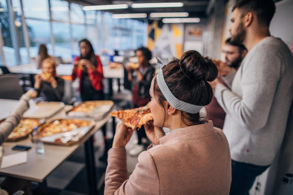 Pracownicy podczas nieformalnego spotkania w biurze jedzą wspólnie pizzę i rozmawiają ze sobą