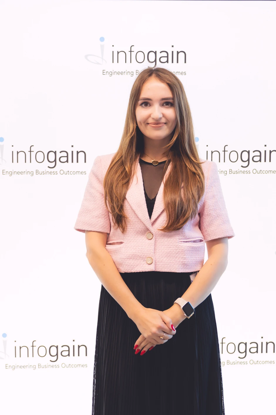 Młoda kobieta ubrana elegancko na tle firmowego baneru Infogain z uśmiechem na twarzy