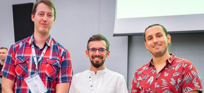 Trzech mężczyzn w casualowych strojach pozujących podczas firmowego wydarzenia z uśmiechami na twarzach