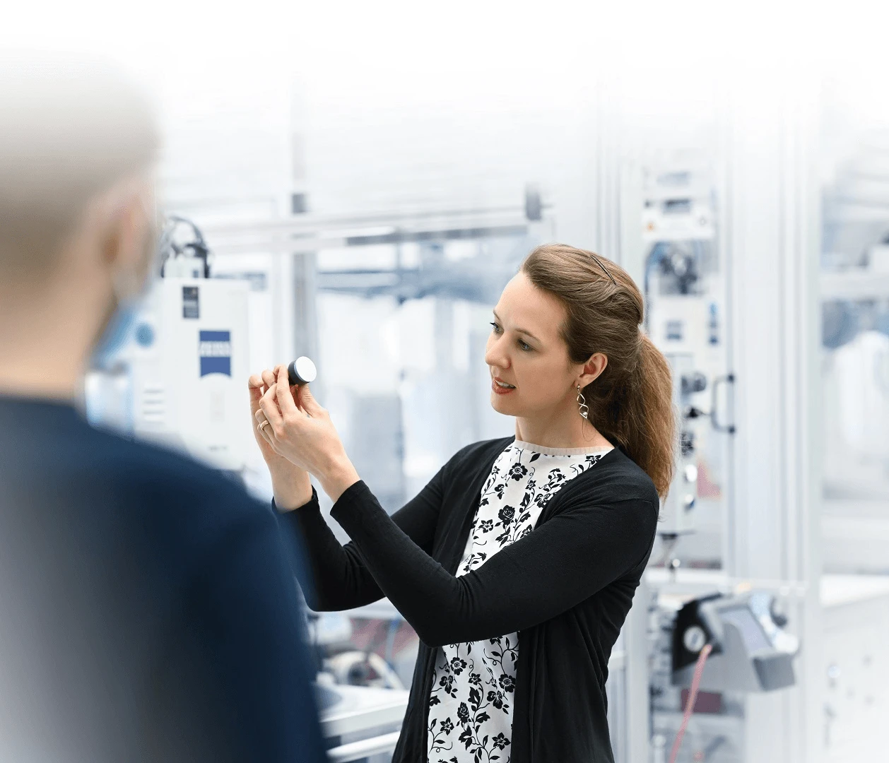 Kobieta prezentuje mały przedmiot w nowoczesnym laboratorium lub zakładzie technicznym podczas pracy zespołowej