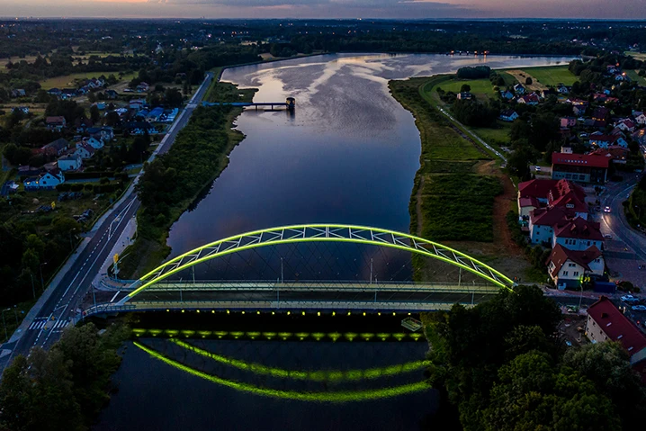 Widok nocny na most oświetlony zielonym światłem nad rzeką z okolicznymi budynkami i drogami