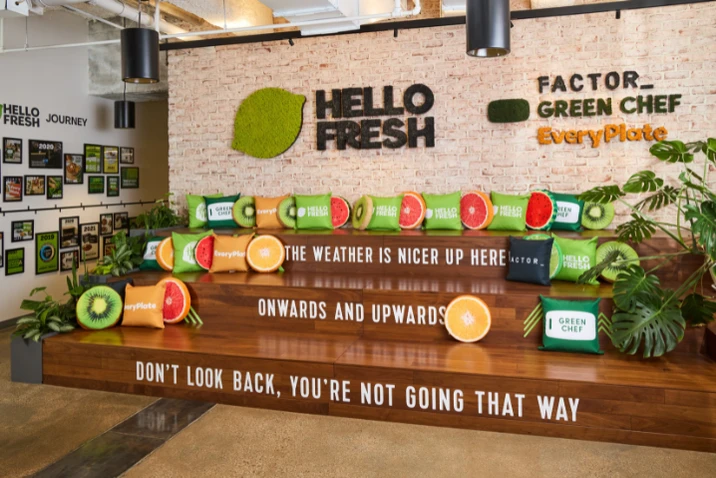 Nowoczesne biuro HelloFresh z kolorowymi poduszkami w kształcie owoców oraz motywującymi napisami na drewnianych stopniach