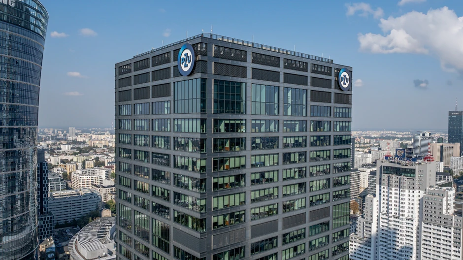 Nowoczesny wieżowiec z logo PZU w centrum miasta pod jasnym, niebieskim niebem