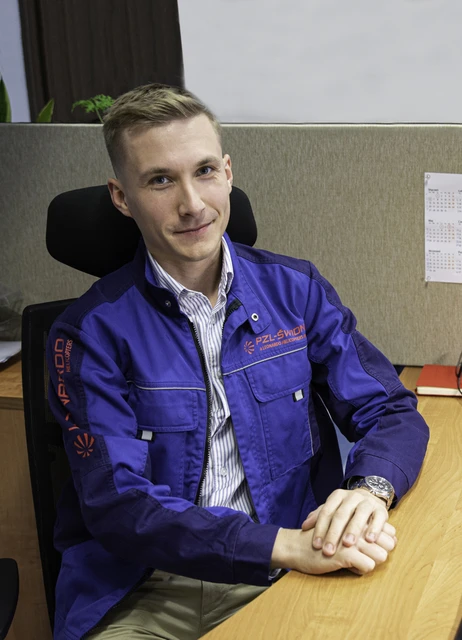 Młody mężczyzna w stroju roboczym z logo PZL-Świdnik siedzi przy biurku w nowoczesnym biurze