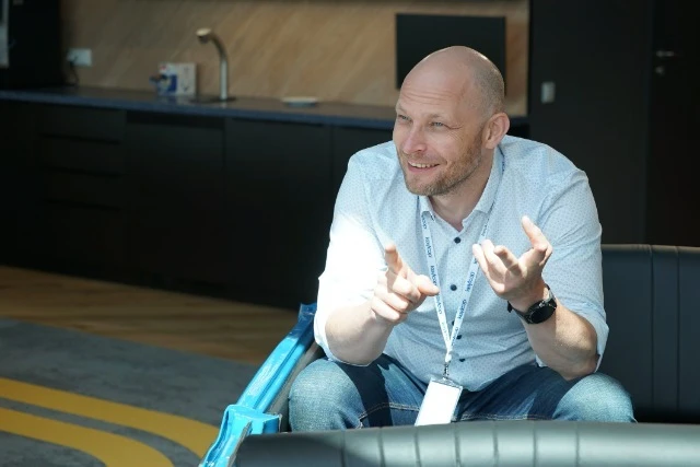 Mężczyzna w koszuli z identyfikatorem prowadzi rozmowę w nowoczesnym, jasnym biurze firmowym