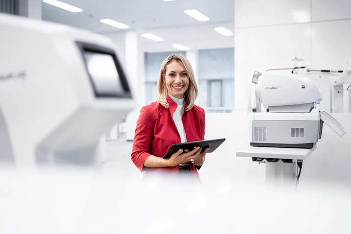 Uśmiechnięta kobieta w czerwonej marynarce pracuje na tablecie w nowoczesnym, jasnym laboratorium