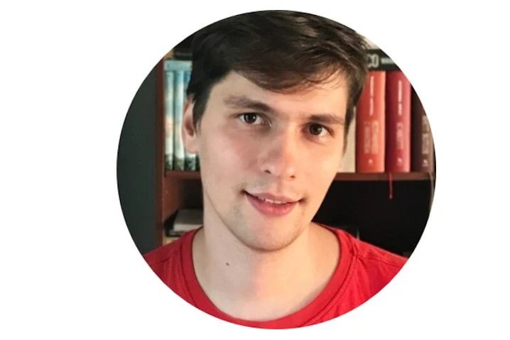 Portret młodego mężczyzny w czerwonej koszulce na tle półki z książkami w biurze