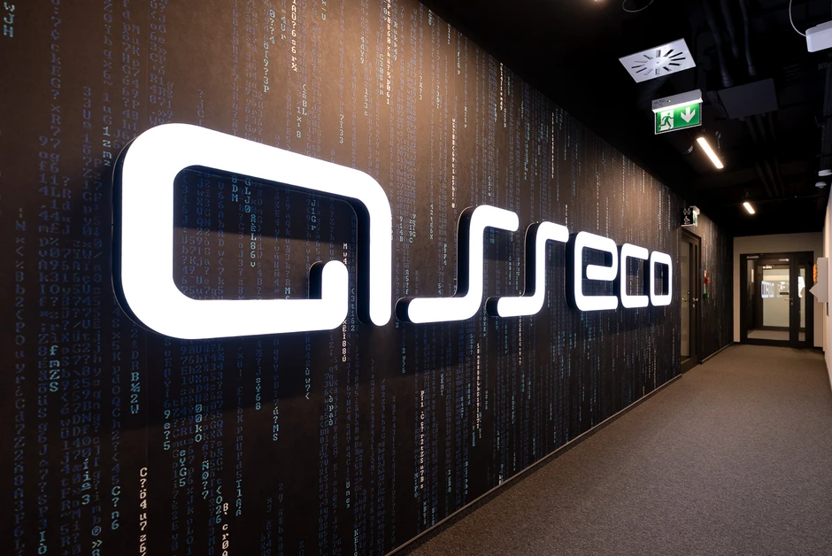Jasne logo Asseco na ścianie z motywem cyfr i liter w nowoczesnym korytarzu biurowym