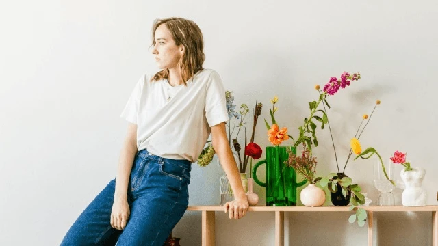 Kobieta opiera się o stół z bukietem kolorowych kwiatów w jasnym minimalistycznym wnętrzu