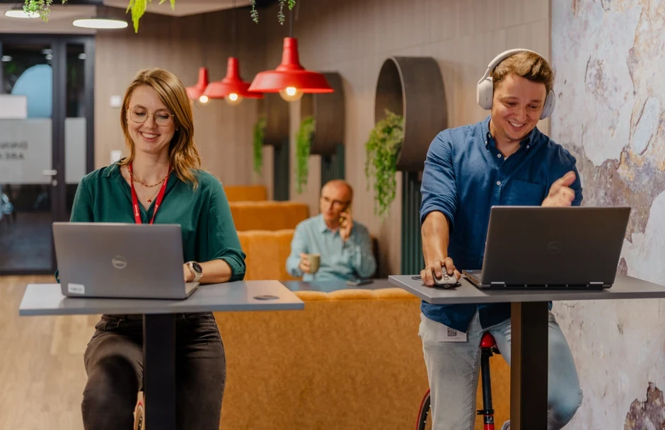 Dwójka pracowników korzysta z laptopów stojąc przy biurkach w nowoczesnej, inspirującej przestrzeni biurowej