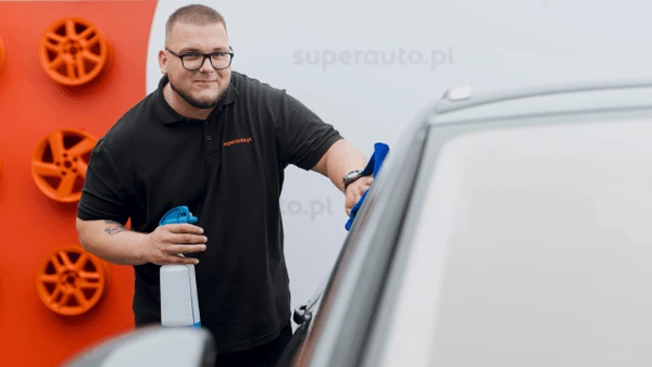 Pracownik firmy superauto.pl czyści karoserię samochodu na tle czerwonej ściany z felgami