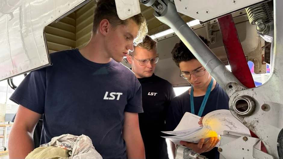 Trzech pracowników w koszulkach LST analizuje dokumentację techniczną przy mechanizmie maszyny