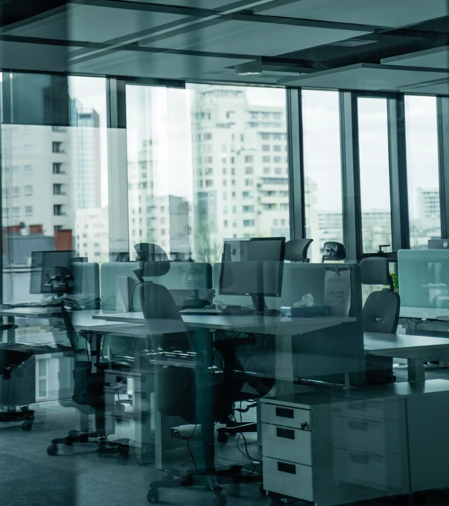 Nowoczesne biuro z komputerami i ergonomicznymi fotelami z widokiem na miejskie wieżowce przez duże okna