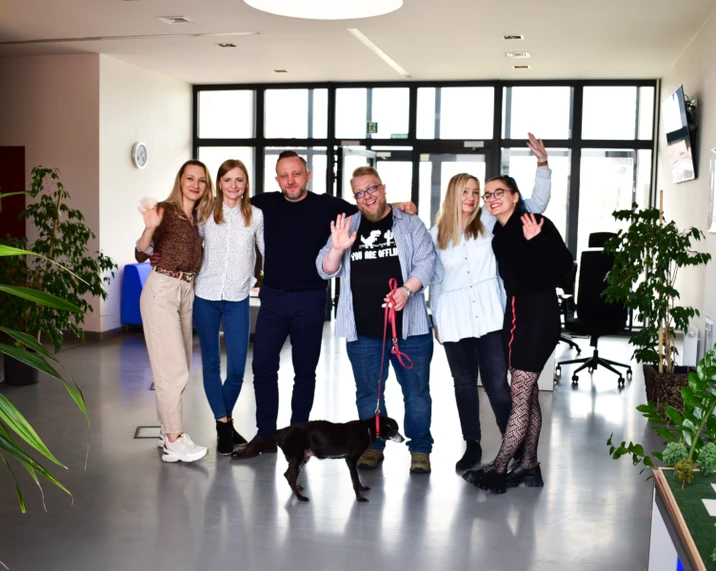 Zespół pracowników biurowych pozujący uśmiechnięty z psem w nowoczesnym, jasnym biurze