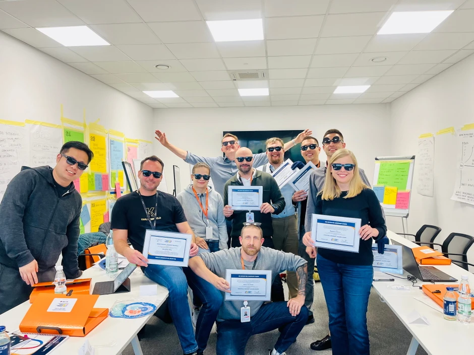 Zespół pracowników w biurze świętuje zdobycie certyfikatów trzymając je i nosząc okulary przeciwsłoneczne