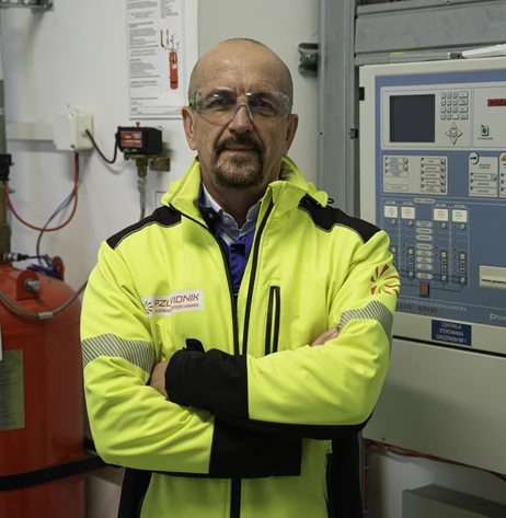 Mężczyzna w żółtej kurtce ochronnej stoi w pomieszczeniu technicznym przy urządzeniach kontrolnych