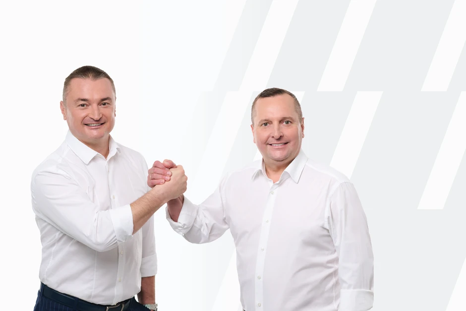 Dwóch mężczyzn w białych koszulach uśmiecha się i ściska dłonie na jasnym tle z grafiką