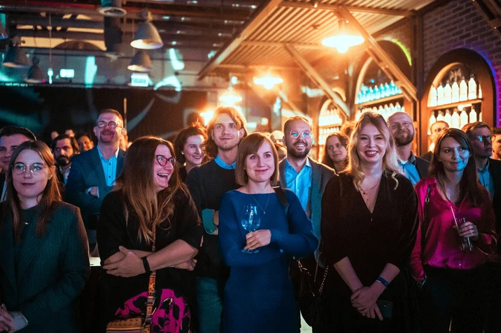 Grupa uśmiechniętych pracowników uczestniczy w firmowym wydarzeniu w stylowym wnętrzu z ciepłym oświetleniem