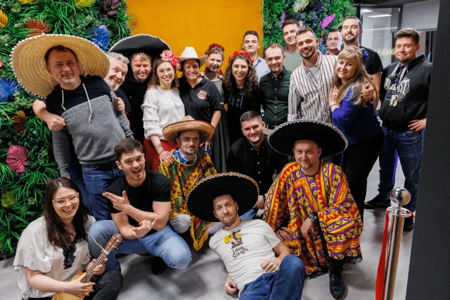 Grupa pracowników w kolorytowych strojach i kapeluszach świętuje razem wydarzenie firmowe w biurze