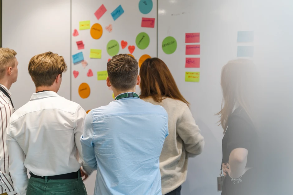 Grupa młodych pracowników omawia pomysły zapisane na kolorowych karteczkach na ścianie w biurze